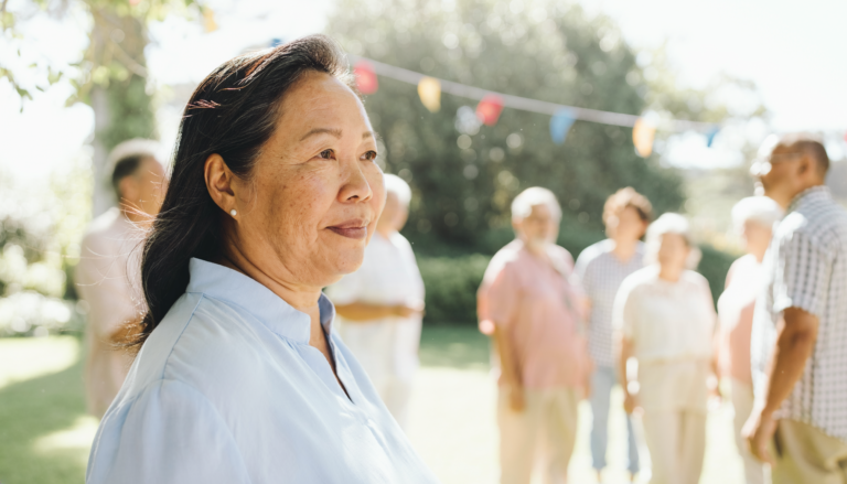 A woman in a pale blue blouse standing apart from a garden gathering.